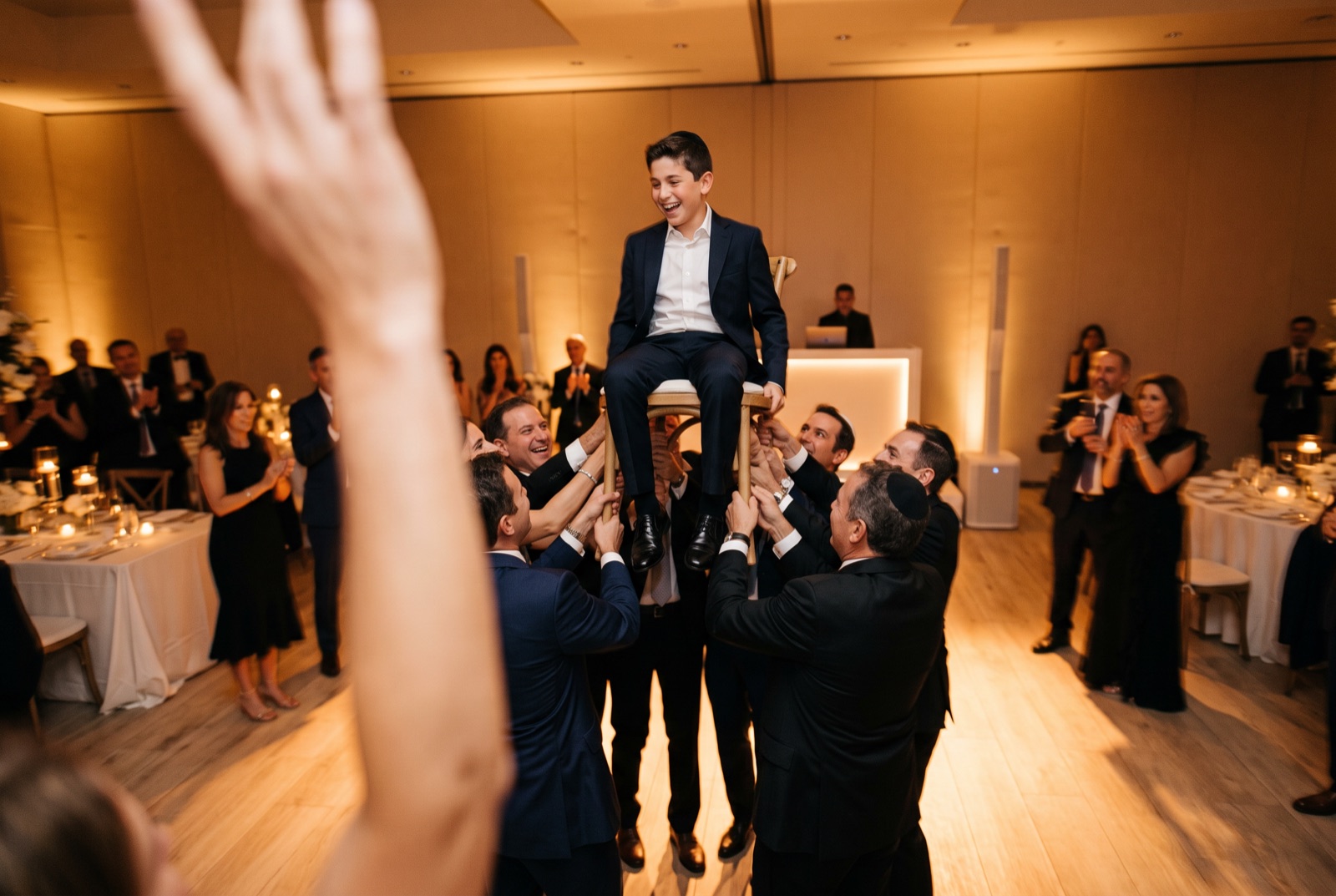 Guests lifting the bar mitzvah boy on a chair during the hora at a Miami simcha