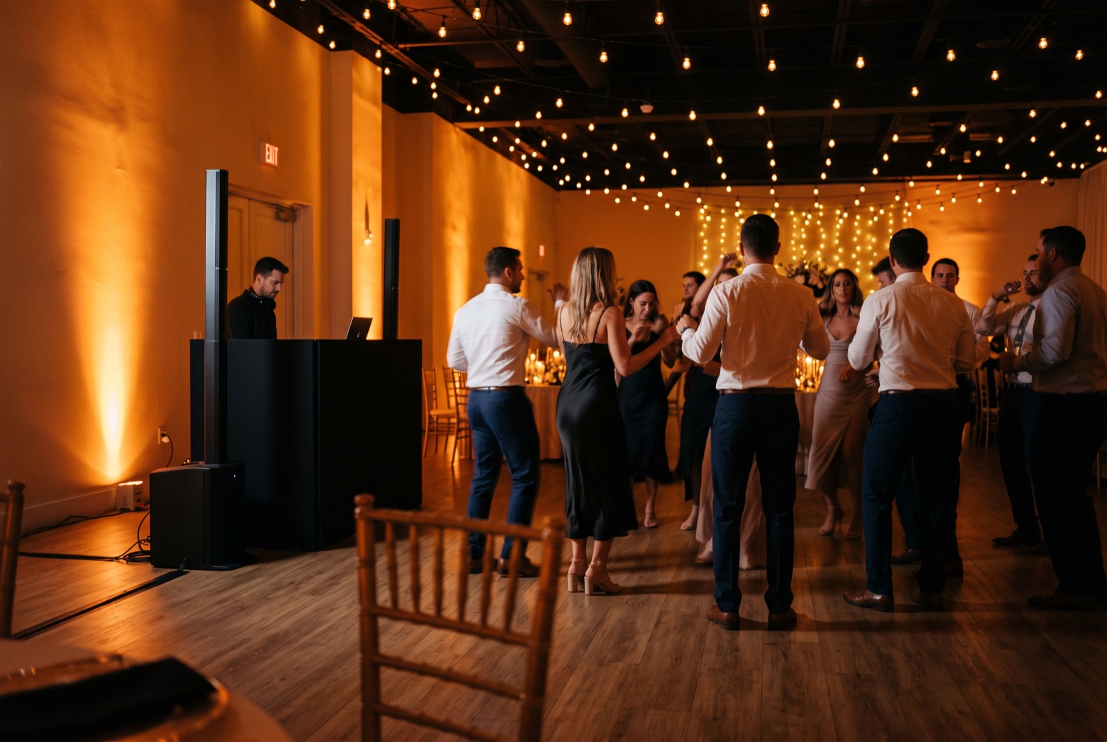 Wedding reception in a Miami ballroom with a lit stage backdrop, uplighting, and a full dance floor